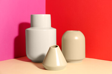 Stylish empty ceramic vases on color background