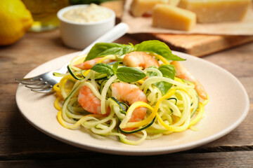 Delicious zucchini pasta with shrimps and basil on wooden table, closeup