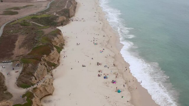 AERIAL: half moon bay beach cliffs and people walking on the beach, drone view