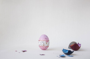 On a white background, a painted pink egg and a multi-colored shell. Holiday and joy of Bright Easter for the whole family. A real hand-painted egg. Multifaceted photo.