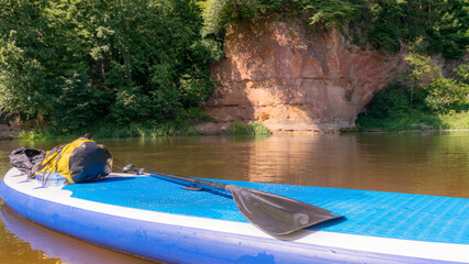 sunny day on the river, stand up board on the river bank, tree reflections in the water, blue sky...