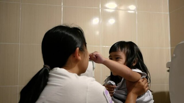 Mother held her daughter and sat on the toilet. Toilet training for toddler with mom.