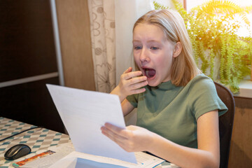 The blonde teen girl looking at and holding paper and read something with surprised face. Emotions of surprise.