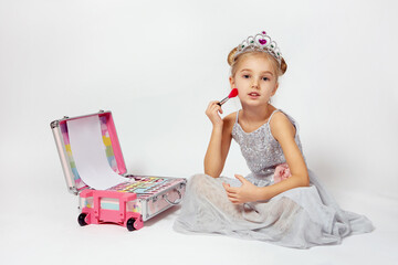A little girl in a shiny Princess costume is sitting next to a large makeup bag.