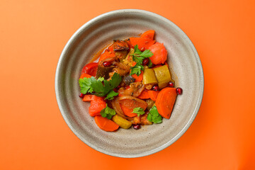 Baked vegetable salad in a cermaic bowl over orange background. Delicious healthy autumn or winter salad.