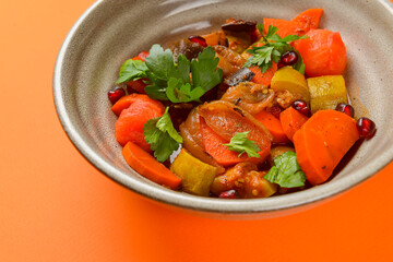 Baked vegetable salad in a cermaic bowl over orange background. Delicious healthy autumn or winter salad.