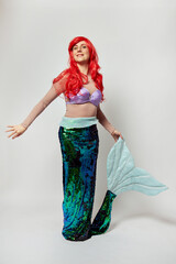A young woman in a bright mermaid costume with red hair. Costume party or Halloween. White...