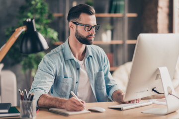 Photo portrait of smart guy taking notes working on computer at desk in modern industrial office...