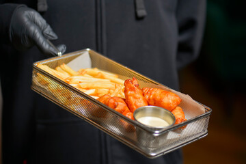 Fried chicken and french fries in metal tray served by waiter in restaurant or diner. Eating out, fast food concept.