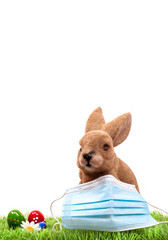 Easter bunny with surgical mask on green grass with easter eggs. Rabbit, Easter holiday 2021 during...