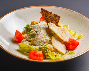 Bowl of Caesar Salad served on a black background in restaurant or diner. Traditional Caesar recipe