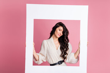 Photo portrait of cheerful woman keeping photo frame wearing summer dotted white dress isolated pastel pink color background
