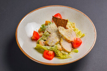Bowl of Caesar Salad served on a black background in restaurant or diner. Traditional Caesar recipe