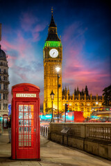 Fototapeta na wymiar Red telephone booth in front of the illuminated Big Ben clocktower in London, United Kingdom, just after sunset with street traffic