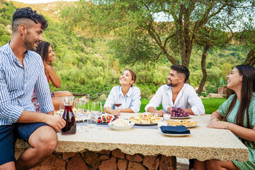 Group of young mixed-race people having fun outdoor in the countryside eating snacks and drinking...