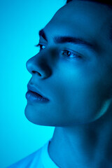 Calm. Handsome caucasian man's portrait isolated on blue studio background in neon, monochrome. Beautiful male model. Concept of human emotions, facial expression, sales, ad, fashion and beauty.