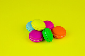 Plastic rainbow macaroons close up on trendy yellow modern fashion background. Toy colored small cakes on yellow background top view, banner