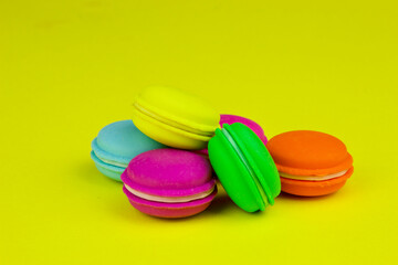 Plastic rainbow macaroons close up on trendy yellow modern fashion background. Toy colored small cakes on yellow background top view, banner