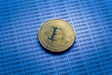 Selective focus of gold bitcoin on a paper of binary code.