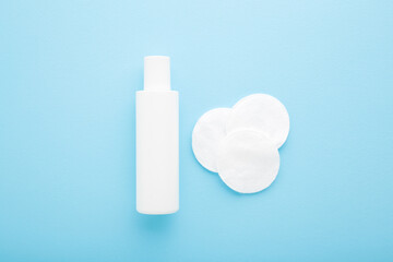 White soft cleansing cotton pads and plastic bottle on light blue table background. Pastel color. Closeup. Simple set for face makeup or nails polish removing. Top down view.