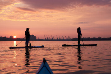 Silhouettes a boy and girl standing on SUP stand up paddle board during a beautiful winter sunrise on the river