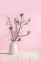 Interior table decoration with branches and hearts in vase on the pink background with copy space
