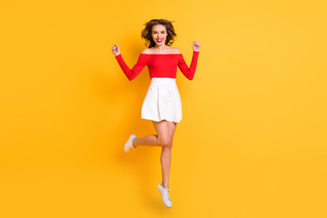 Full length body size photo smiling girl wearing red top white skirt jumping high isolated on bright yellow color background