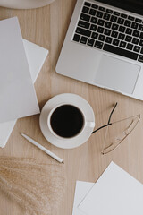 Female home office desk workspace with coffee cup, laptop, glasses, pampas grass on wooden table....