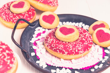 Pink glazed donut and cookies with hearts on a metal tray on a white table
