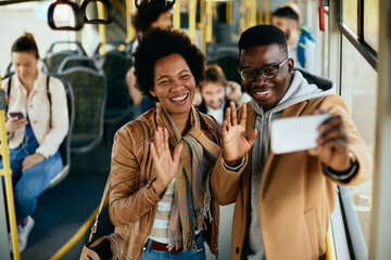 Fototapeta na wymiar Happy black couple waving while having video call in a public transport.