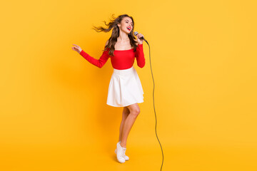 Full length body size of female pop star singing song on stage keeping microphone isolated on vivid yellow color background