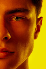 Fototapeta premium Close up. Handsome caucasian man's portrait isolated on orange studio background in neon, monochrome. Beautiful male model. Concept of human emotions, facial expression, sales, ad, fashion and beauty.