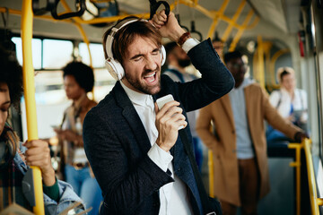 Carefree businessman with headphones singing while traveling by public transport.