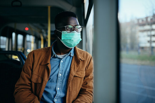African American man with face mask looking through the window while traveling by bus.