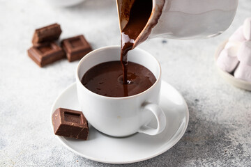 Pouring hot chocolate  from a jug into the cup on white grey background. Winter drink concept.