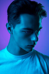 Youth. Handsome caucasian man's portrait isolated on purple studio background in neon, monochrome. Beautiful male model. Concept of human emotions, facial expression, sales, ad, fashion and beauty.