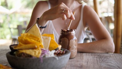 Beautiful young blonde woman enjoys her chocolate milkshake while having lunch alone at a beach restaurant. Solo travel