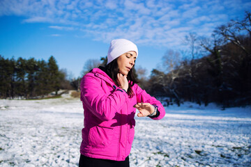 Sportswoman in winter training clothes measuring her pulse after running on snow.