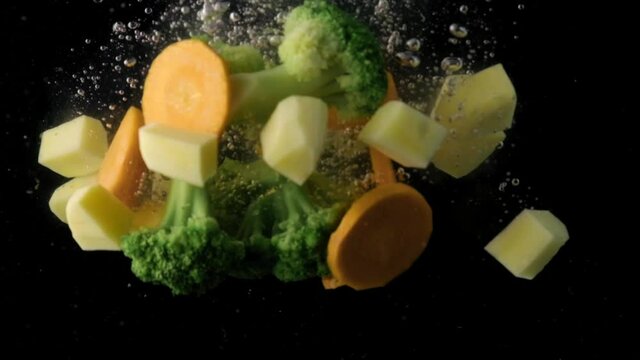 A lot of chopped vegetables soup set falls to the input. Black background. Slow motion.