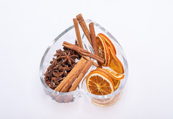 Slices of dried oranges, cinnamon and cardamom in a heart-shaped glass dish