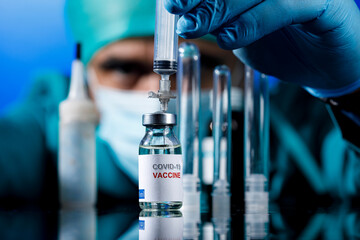 Medico con protezioni mediche e guanti in lattice preleva del il  vaccino anti-covid con una...