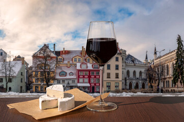 Glass of wine with brie cheese on colorful buildings background in historic city center in Riga, Latvia