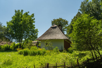 Fototapeta na wymiar Old, medieval, traditional Ukrainian rural house with wicker hedge and garden with flowers.