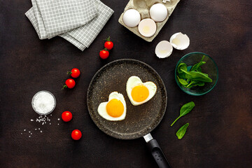 Cooking heart-shaped fried eggs in a pan with tomatoes and greens