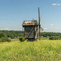 Old windmill and medieval, traditional Ukrainian rural houses on a green meadow. Blue sky with white clouds.