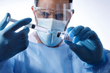 Medico con mascherina chirurgica ,guanti in lattice , maschera e camice,  preleva il vaccino...