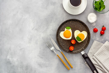 Cooking heart-shaped fried eggs in a pan with tomatoes and greens