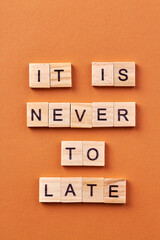 Phrase made of wooden cubes. Its never too late orange background vertical shot.