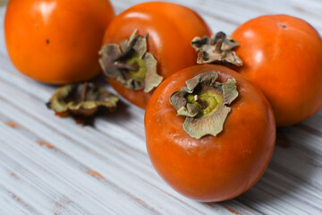 Fresh ripe persimmon fruits on a wooden board, winter fruits, light background. Full depth of field