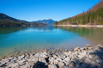 rocky lake shore Walchensee in march, boathouse and alps view